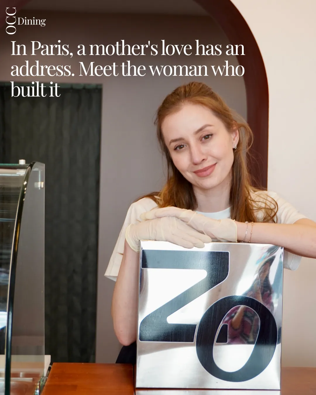 Marina, founder of Café Zo, holding the mirrored ZO sign behind her counter.